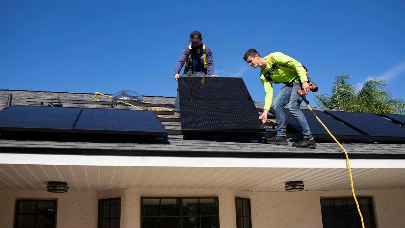 Two installers fitting solar modules on the roof of a house